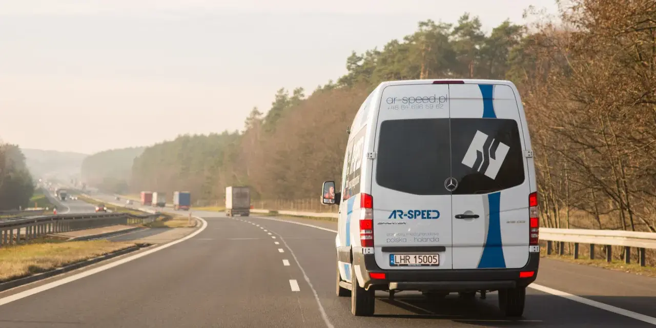 Biały bus AR-SPEED jedzie autostradą. Zastanawiasz się, ile kosztuje bus do Niemiec? Sprawdź na ar-speed.pl.