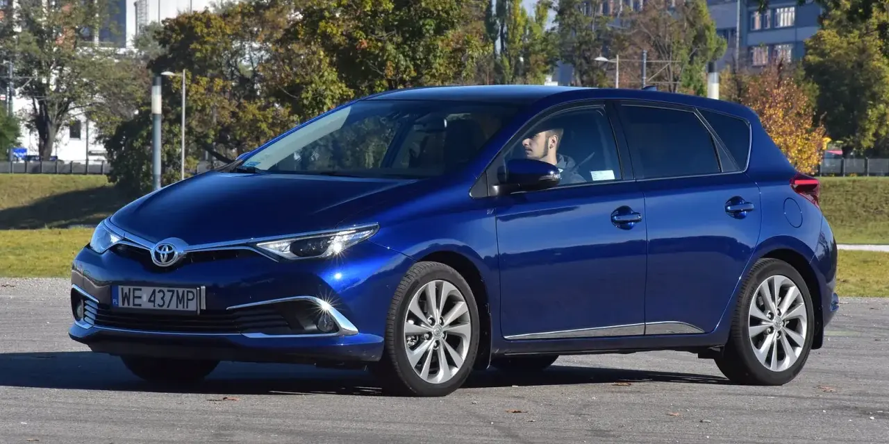Niebieska Toyota Auris Hybrid, z kierowcą za kierownicą, na parkingu. Zastanawiasz się, ile pali Toyota Auris Hybrid?