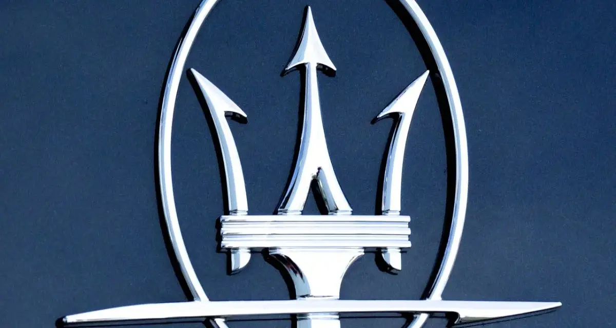 Błyszczący, chromowany trójząb Neptuna, czyli jak wygląda znaczek Maserati, na ciemnoniebieskim tle.