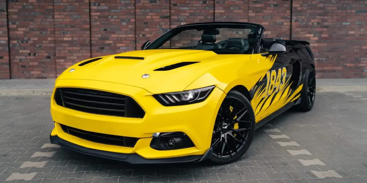 Żółty kabriolet Mustang GT 5.0 z czarnymi felgami i grafiką na boku.