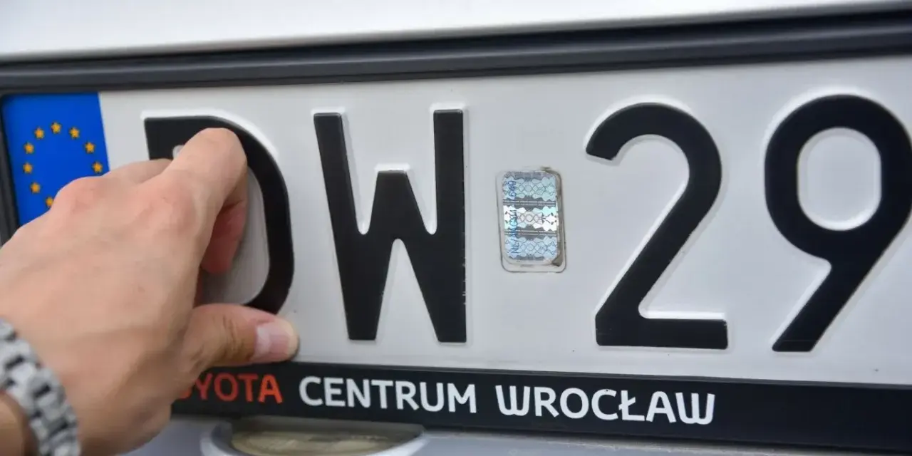 Dłoń dotyka tablicy rejestracyjnej z literami DW i numerem 29. To tablice rejestracyjne województwa dolnośląskiego.