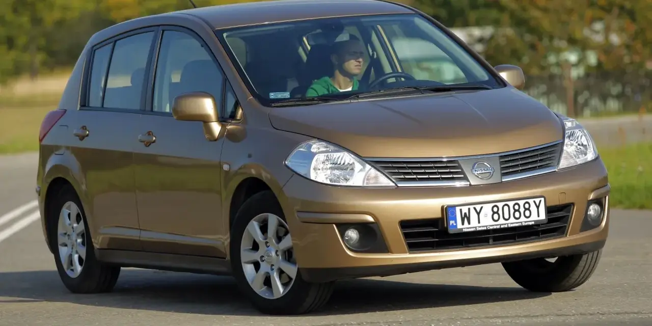 Złoty Nissan Tiida z mężczyzną za kierownicą jedzie po drodze.