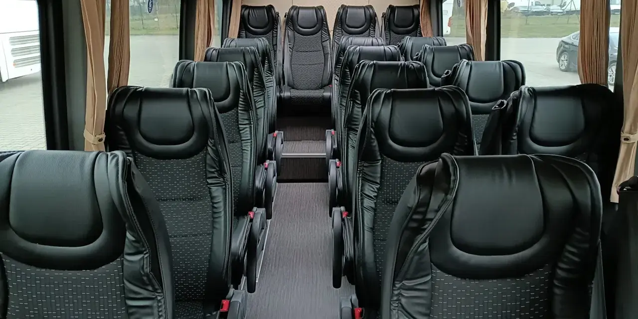 Wnętrze busa z rzędami czarnych, wygodnych siedzeń. Widać, ile miejsc ma bus osobowy, gotowy na podróż.