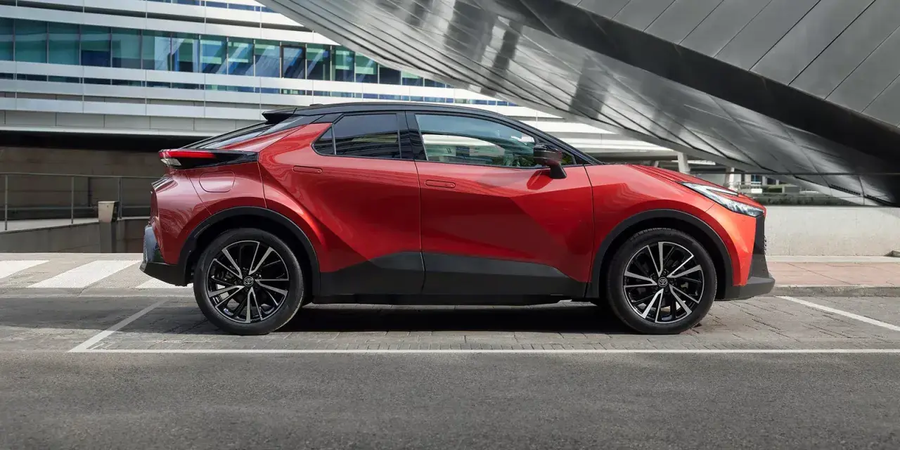 Czerwona Toyota C-HR Hybrid na tle nowoczesnego budynku. Zastanawiasz się, ile kosztuje Toyota C-HR Hybrid?