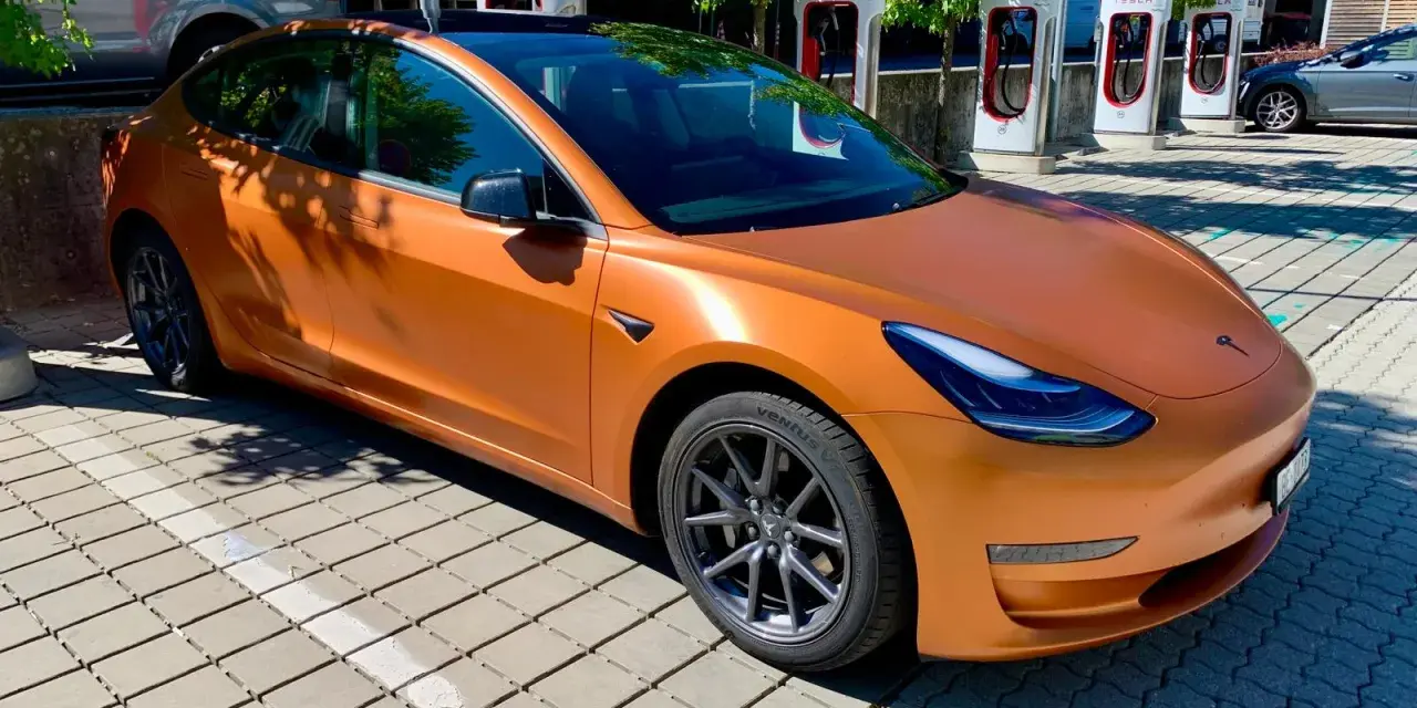 Pomarańczowa Tesla Model 3 na ładowarce. Zastanawiasz się, ile przejedzie Tesla na jednym ładowaniu?
