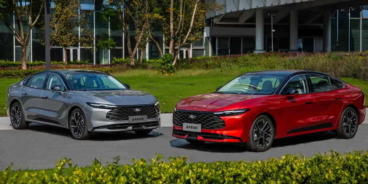 Dwa nowe Fordy Mondeo mk6, jeden czerwony, drugi szary, stoją obok siebie na tle nowoczesnego budynku i zieleni.