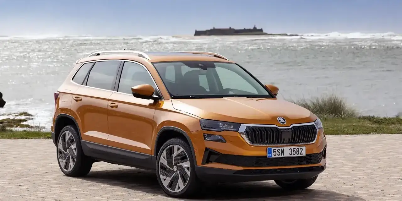 Pomarańczowa Skoda Karoq na tle morza i zamku. Sprawdź aktualny skoda cennik i wybierz swój wymarzony model.