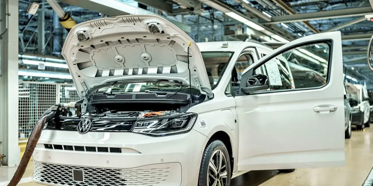 Biały samochód elektryczny na linii produkcyjnej. Widać otwartą maskę i drzwi, a także elementy silnika. Powstają tu polskie samochody.