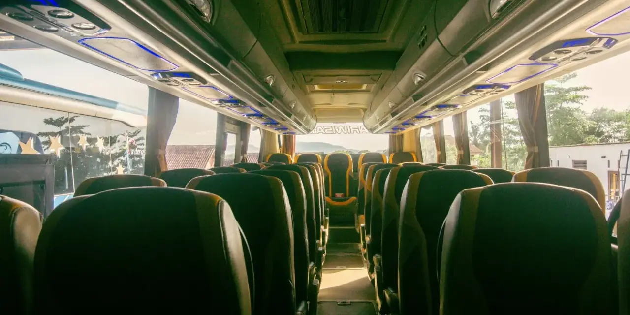 Wnętrze autobusu z rzędami zielonych siedzeń. Trudno ocenić, ile bus ma miejsc, ale wygląda na to, że jest ich sporo.