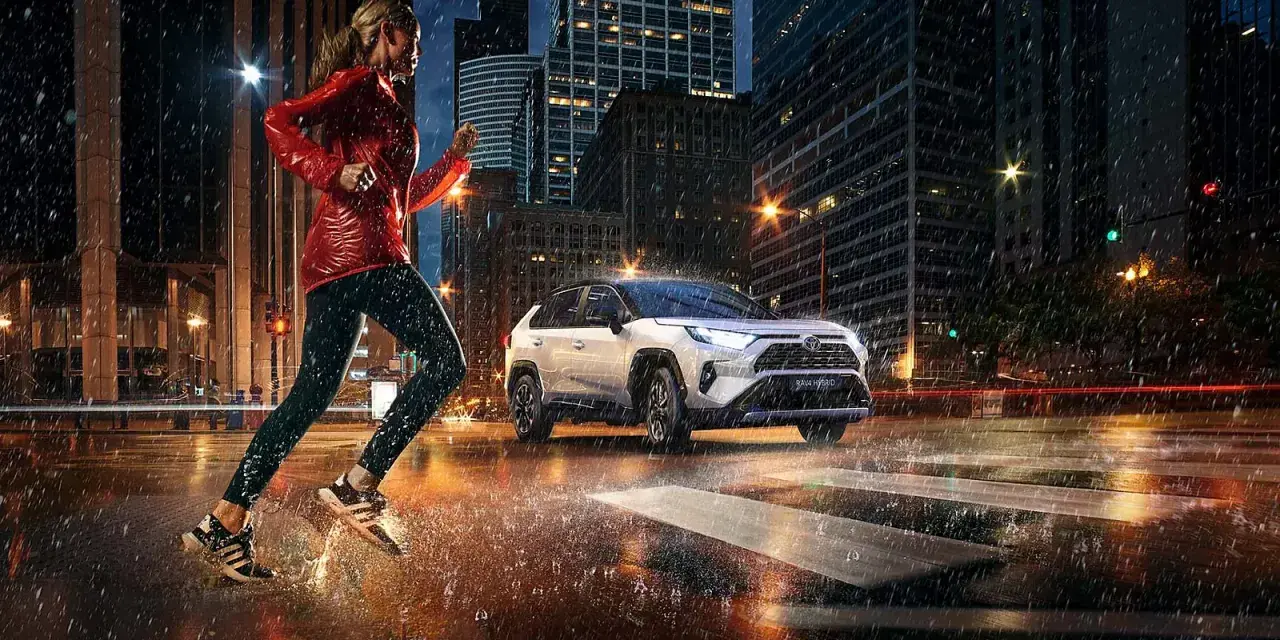 Biegaczka w deszczowy wieczór w mieście, obok niej biała Toyota RAV4 Hybrid. Zastanawiasz się, ile pali Toyota RAV4 Hybrid?