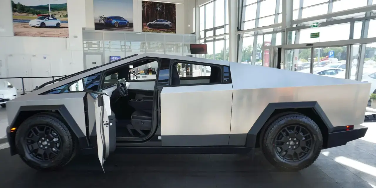 Futurystyczny Cybertruck z otwartymi drzwiami stoi w salonie. Jego kanciasta, metaliczna karoseria przyciąga wzrok.