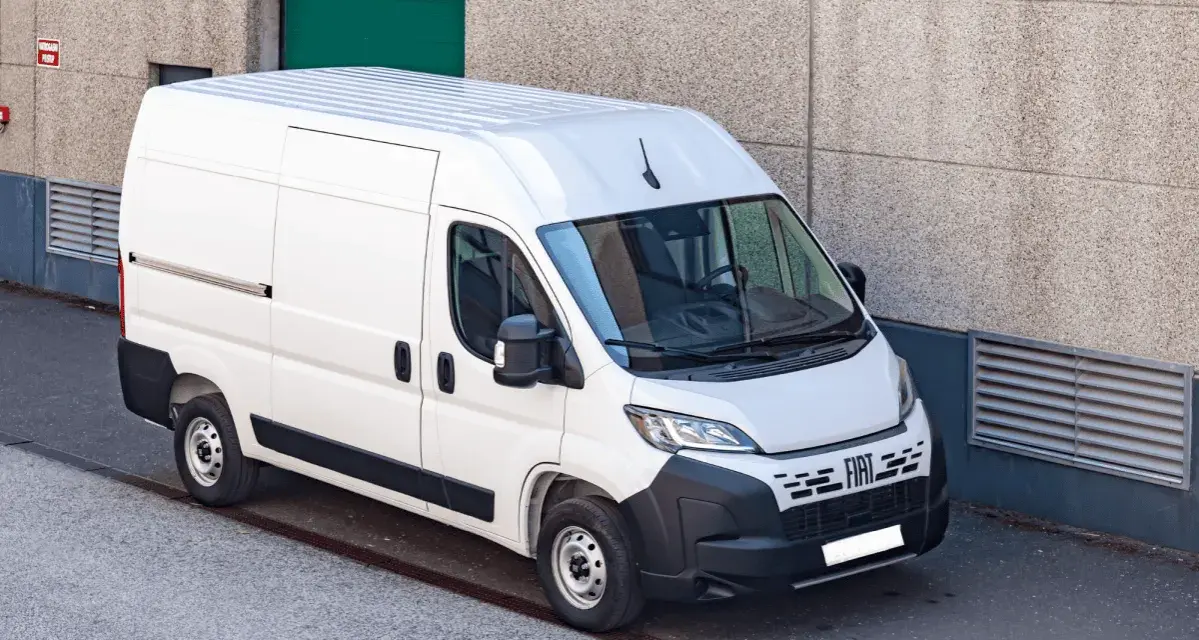 Biały bus 9 osobowy Fiat Ducato, zaparkowany przy betonowej ścianie. Zastanawiasz się, ile pali bus 9 osobowy?