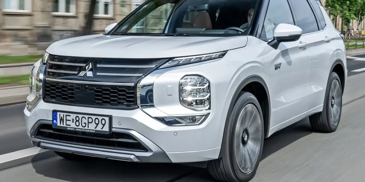 Biały Mitsubishi Outlander PHEV, jeden z nowoczesnych modeli tej marki, jedzie po mieście.