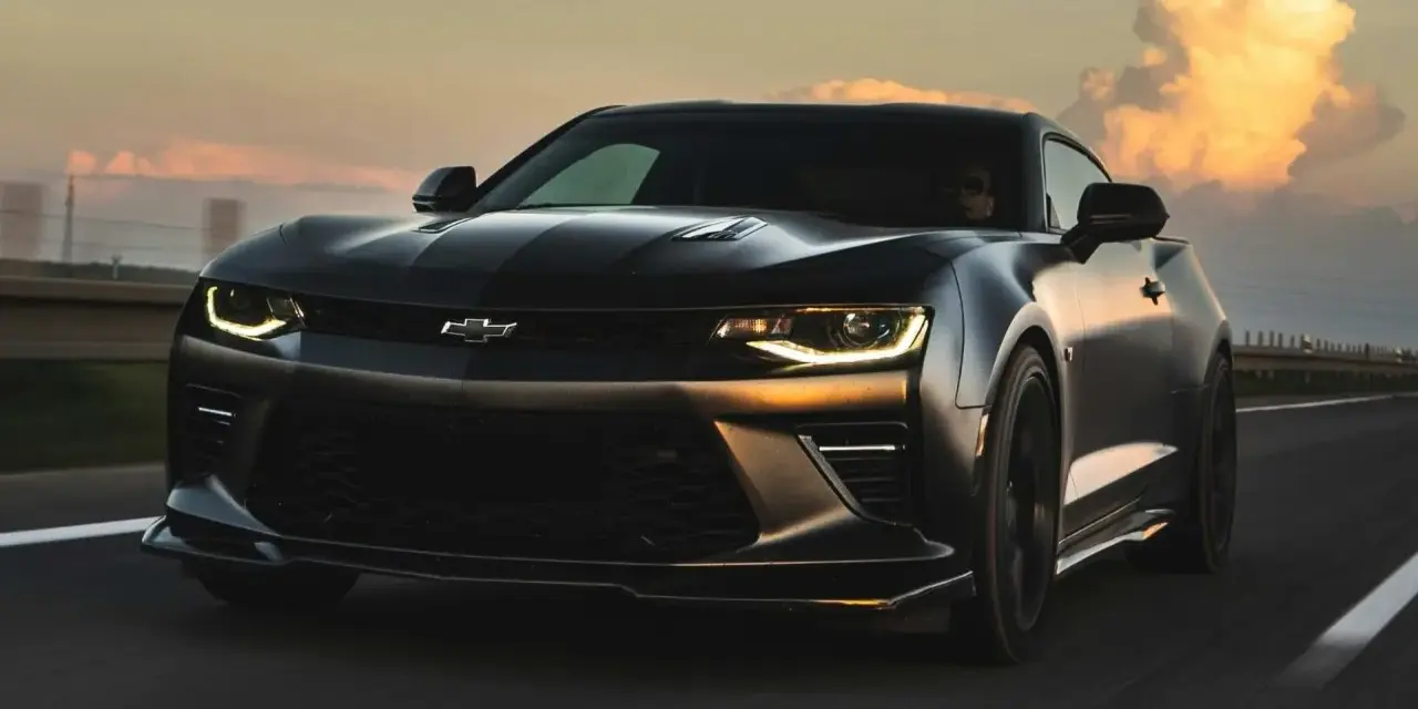 Czarny Chevrolet Camaro pędzi po autostradzie o zachodzie słońca.