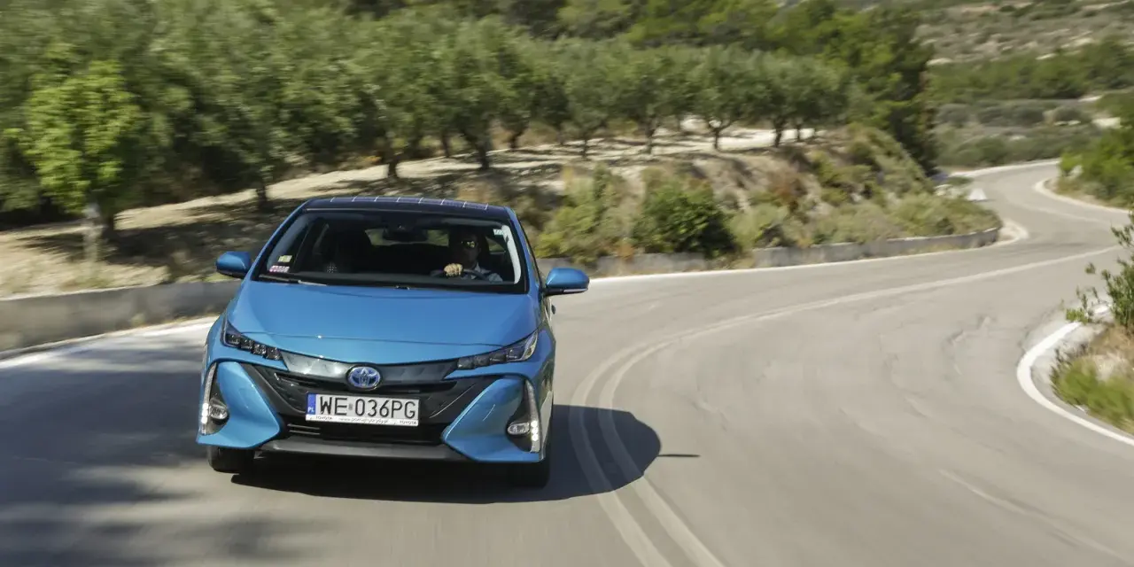 Niebieska Toyota Prius pokonuje zakręt na malowniczej drodze. Zastanawiasz się, ile pali Toyota Prius? Ten model jest znany z oszczędności.