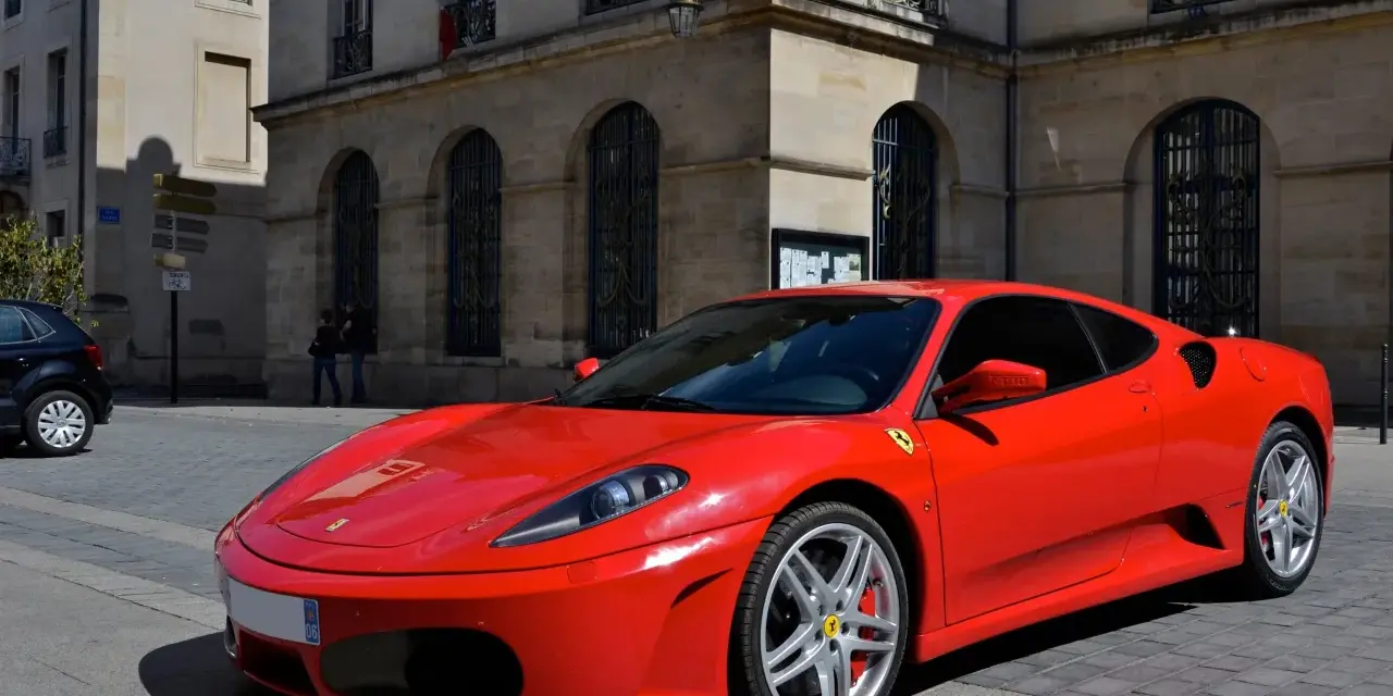 Czerwone Ferrari F430 na brukowanej ulicy przed kamienicą. Zastanawiasz się, ile kosztuje najtańsze Ferrari?