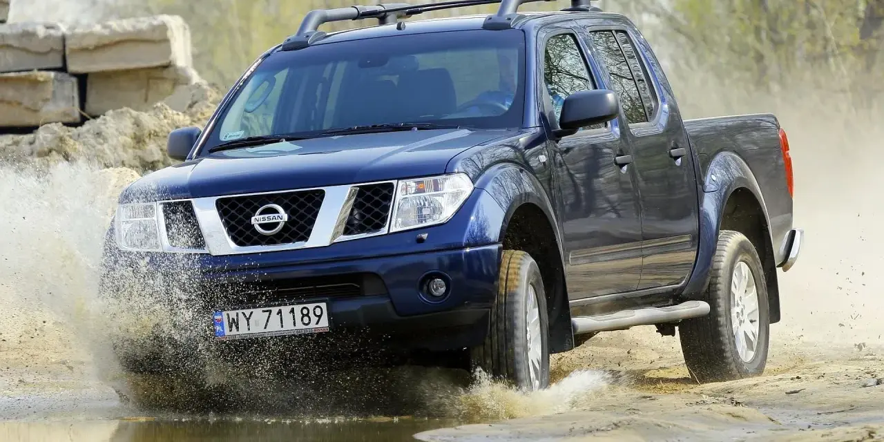 Niebieski Nissan Navara pokonuje wodną przeszkodę, wzbijając fontanny błota.