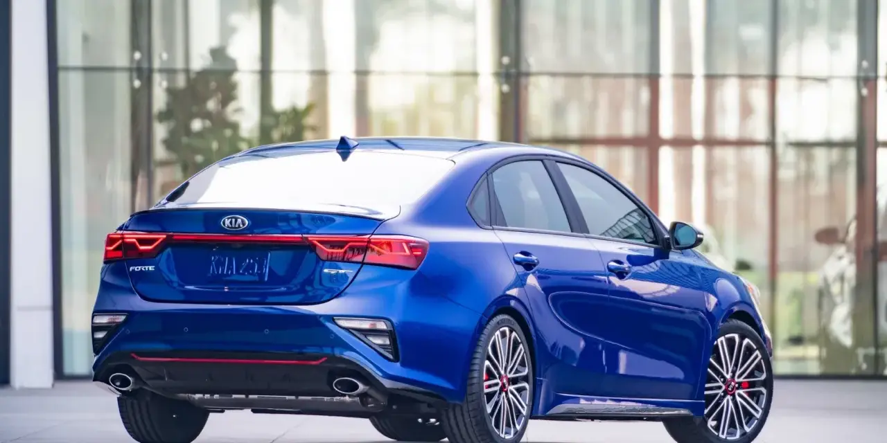 Niebieskie Kia Forte GT z czerwonymi akcentami, zaparkowane przed nowoczesnym budynkiem.