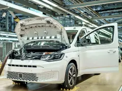 Biały samochód elektryczny na linii produkcyjnej. Widać otwartą maskę i drzwi, a także elementy silnika. Powstają tu polskie samochody.