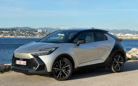 Srebrno-czarna Toyota C-HR na tle morza i miasta. Zastanawiasz się, ile przejedzie hybryda Toyoty na jednym ładowaniu?