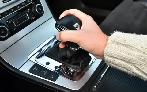 Dłoń trzyma gałkę zmiany biegów w samochodzie. Widoczna jest automatyczna skrzynia biegów DSG z przyciskami ESP, Auto Hold i czujnikami parkowania.