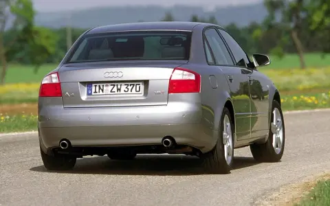 Srebrne Audi B6 sedan z tablicą rejestracyjną IN ZW 370 jedzie po asfaltowej drodze wśród zieleni i żółtych kwiatów.
