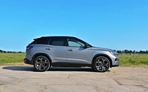 Srebrny Renault Austral z czarnym dachem stoi na polnej drodze. W tle zielone pole i las.
