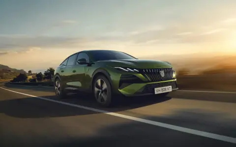 Zielony Peugeot 408 GT sunie po krętej drodze, otoczony malowniczym krajobrazem o zachodzie słońca.