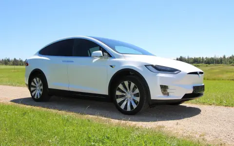 Biała Tesla Model X na tle łąki i lasu. Zastanawiasz się, ile kosztuje najtańsza Tesla?