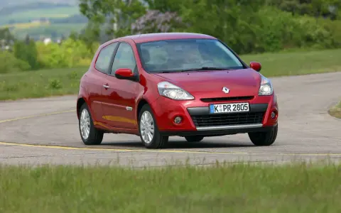 Czerwony Clio 3 na zakręcie drogi, otoczony zielenią.