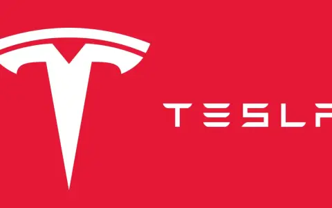 Biały, stylizowany symbol litery "T" i napis "TESLA" na czerwonym tle. Tak wygląda znaczek Tesli.