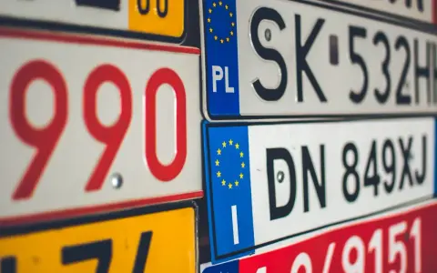Zbliżenie na stos tablic rejestracyjnych z różnymi kody samochodowe. Widoczne numery to m.in. 990, SK 532HH, DN 849XJ.