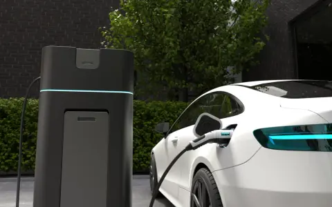 Biała Tesla ładuje się przy nowoczesnej stacji. Wyświetlacz pokazuje "CHARGING 100%", odpowiadając na pytanie, jak długo ładuje się Tesla.