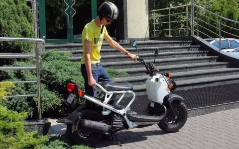 Chłopak w kasku i żółtej koszulce przy białym skuterze. Zastanawiasz się, ile kosztuje karta motorowerowa?