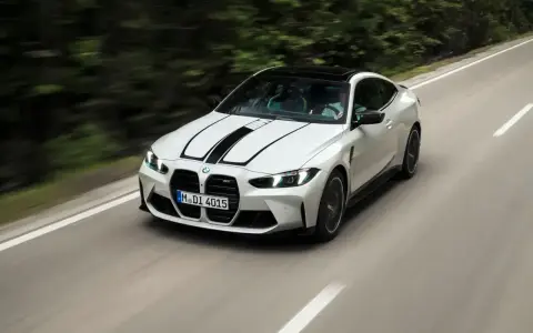 Białe BMW M4 z czarnymi pasami na masce pędzi po krętej drodze. Zastanawiasz się, ile kosztuje BMW M4?