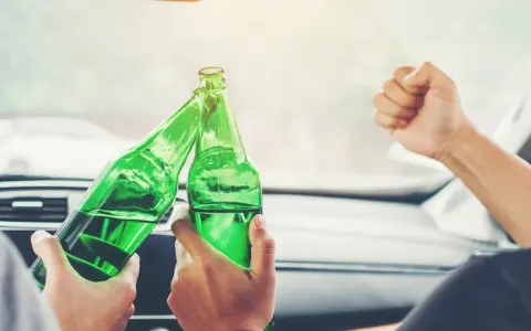 Dwie osoby w samochodzie wznoszą toast zielonymi butelkami. To nie jest dopuszczalna ilość alkoholu podczas jazdy.
