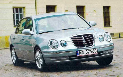 Srebrny Kia Opirus z polskimi tablicami rejestracyjnymi WN 37560 na brukowanej ulicy.