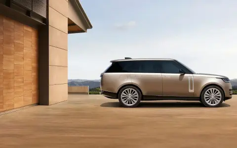 Elegancki Range Rover w kolorze piaskowym, zaparkowany przed nowoczesnym domem z drewnianymi drzwiami. Sprawdź range rover cena!