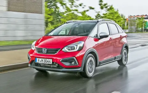 Czerwony Honda Jazz 4 w wersji Crosstar z czarnym dachem i relingami, porusza się po mokrej drodze.