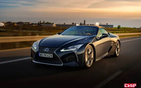 Ciemny Lexus LC 500 z beżowym dachem sunie po drodze podczas zachodu słońca. Sprawdź jego lexus lc 500 cena.