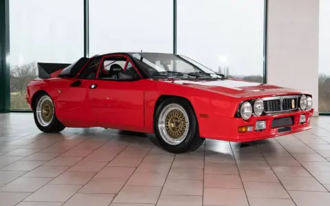 Czerwona Lancia 037 z czarnym spojlerem i złotymi felgami, gotowa do rajdu.
