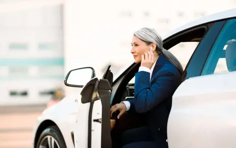 Elegancka kobieta w garniturze wsiada do białego auta. To jej auto na abonament, idealne do biznesowych podróży.