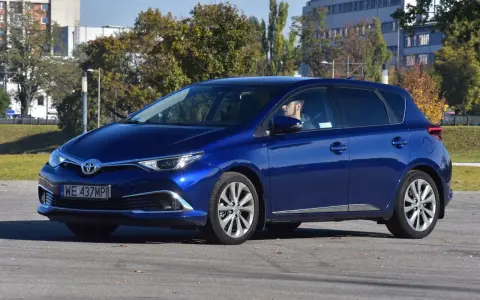 Niebieska Toyota Auris Hybrid, z kierowcą za kierownicą, na parkingu. Zastanawiasz się, ile pali Toyota Auris Hybrid?