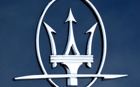 Błyszczący, chromowany trójząb Neptuna, czyli jak wygląda znaczek Maserati, na ciemnoniebieskim tle.