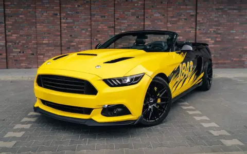 Żółty kabriolet Mustang GT 5.0 z czarnymi felgami i grafiką na boku.