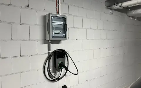 Nowoczesne gniazdo do ładowania samochodu elektrycznego Autel zamontowane na białej, ceglanej ścianie obok skrzynki z bezpiecznikami.