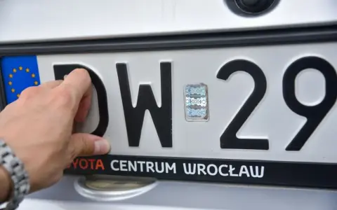 Dłoń dotyka tablicy rejestracyjnej z literami DW i numerem 29. To tablice rejestracyjne województwa dolnośląskiego.