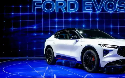 Biały Ford Evos na niebieskim, futurystycznym tle z siatką. Elegancka linia nadwozia i sportowe detale podkreślają jego nowoczesny charakter.