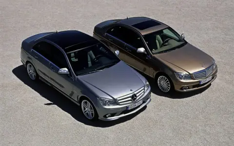 Dwa Mercedesy klasy C W204, jeden srebrny, drugi brązowy, stoją obok siebie na żwirowym placu.