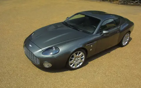 Szary Aston Martin DB9 na żwirowym podjeździe. Zastanawiasz się, ile kosztuje Aston Martin? To auto to marzenie wielu.